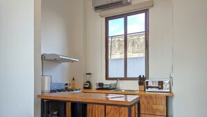 Una cocina compacta con encimera de madera, dos taburetes de bar, un ventanal y un horno empotrado.