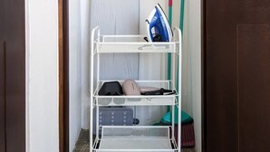 Zona de lavandería con tabla de planchar, un tendedero de metal con ropa doblada y productos de limpieza.