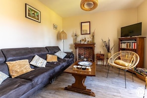 Una sala de estar con sofá, una mesa de centro, una silla de mimbre, una chimenea y una estantería.