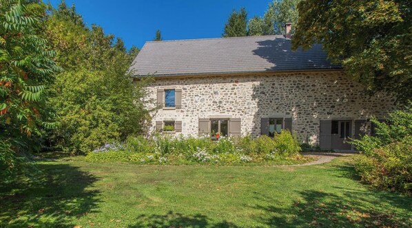 A stone house with a sloped roof, a small front porch, and a well-maintained garden.