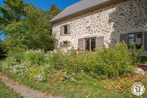 A stone building with shutters, surrounded by greenery and trees.