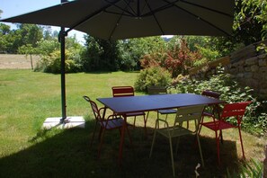Un patio con una mesa, sillas, una sombrilla y un muro de piedra.