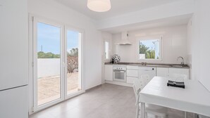 A modern kitchen with white cabinetry, a dining table, and a large sliding glass door leading to an outdoor area.