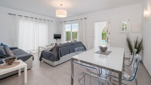 A modern, well-lit room with a bed, a dining table with chairs, a TV, and a view of the outdoors.
