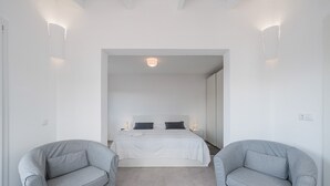 A bedroom with a bed, two grey armchairs, and a white ceiling light.