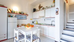 A compact kitchen with white cabinets, a dining table with chairs, a refrigerator, and a microwave. - Holiday Home "Villetta Duplex Breathtaking View" with Sea View, 2 Private Terraces and Wi-Fi (Costa Paradiso)