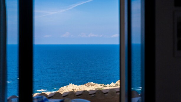A view through a window of a coastal landscape with the sea and rocky shoreline. - Holiday Home "Villetta Duplex Breathtaking View" with Sea View, 2 Private Terraces and Wi-Fi (Costa Paradiso)