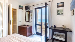 A bedroom with a bed, a dresser, a TV, and a view of the sea through a door. - Holiday Home "Villetta Duplex Breathtaking View" with Sea View, 2 Private Terraces and Wi-Fi (Costa Paradiso)