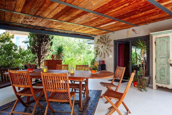 Un espace de restauration en plein air avec une table et des chaises en bois, entouré de plantes en pot et offrant une vue sur la verdure.