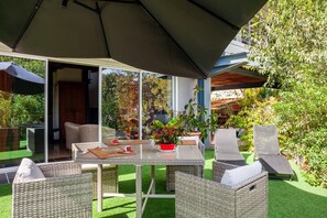 An outdoor patio with wicker furniture, a table with a red pot, and a large umbrella.
