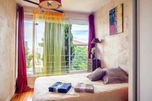 Une chambre à coucher avec un lit, une fenêtre avec des rideaux, une lampe et un tableau au mur.