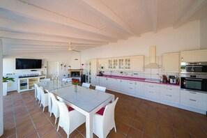 Una cocina amplia con armarios blancos, un comedor con mesa de vidrio y un televisor de pantalla plana montado sobre la encimera.