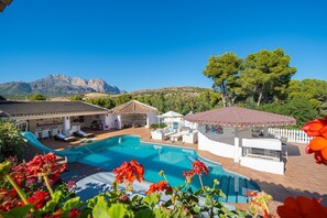 Zona de piscina con sillones de descanso, un espacio cubierto para sentarse y vistas a montañas.