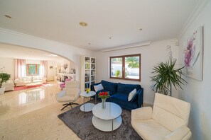 Un salón amplio con un sofá azul, sillones blancos, una mesa de centro y una estantería.