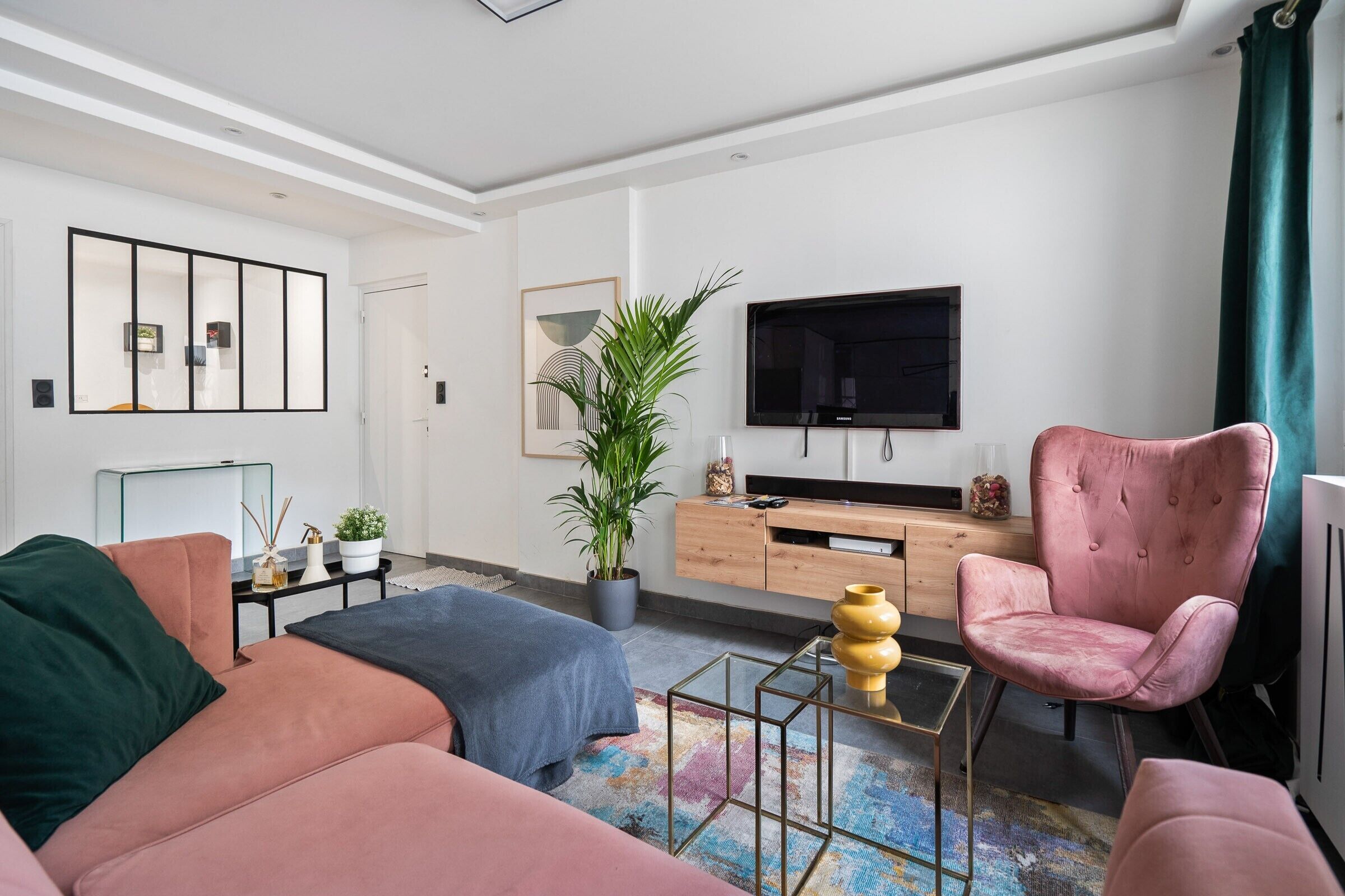 A modern living room with a sofa, armchair, TV, and a potted plant.