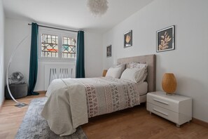 Une chambre à coucher avec un lit, une table de chevet, une lampe et une œuvre d’art accrochée au mur.