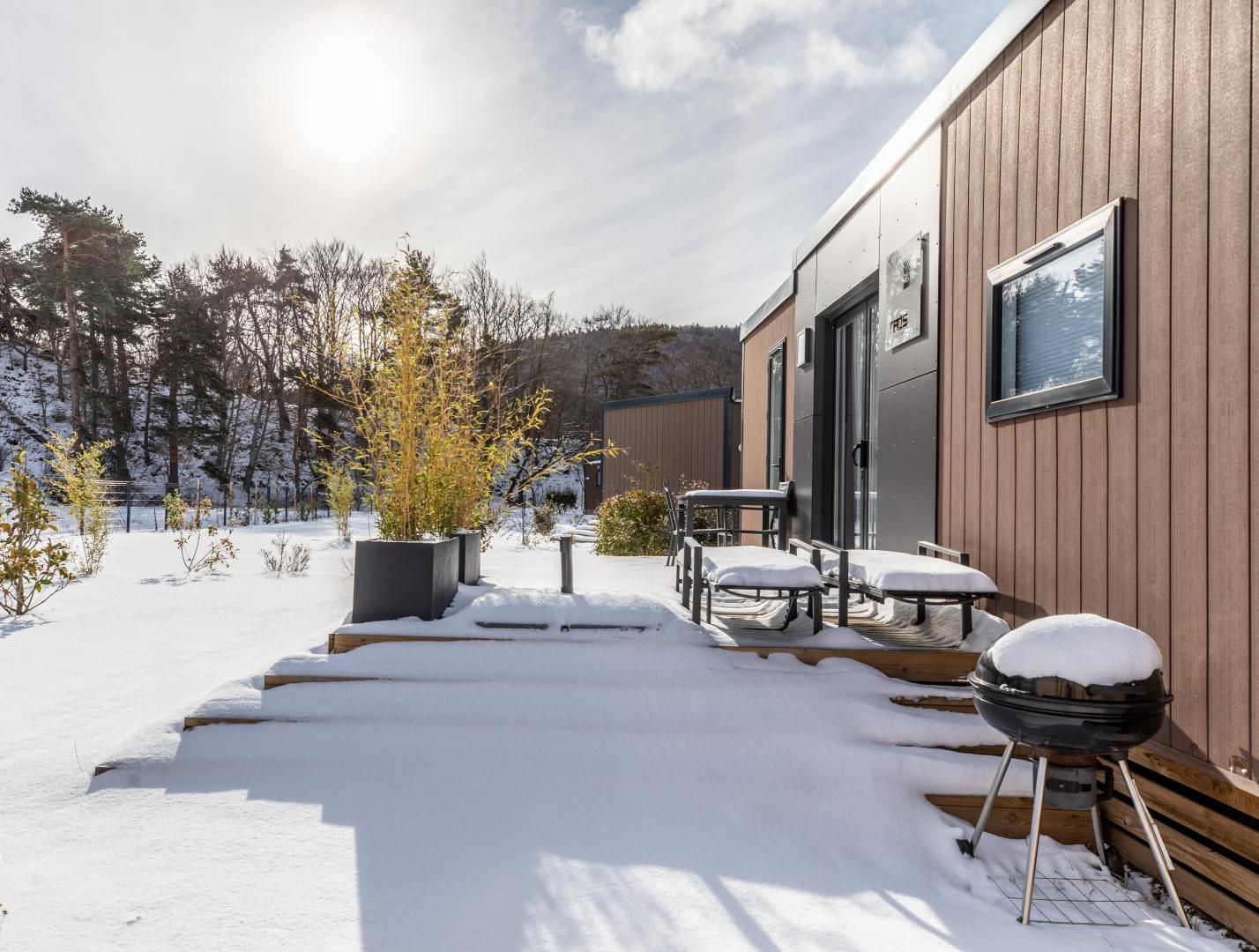 A modern building with a wooden exterior, a covered outdoor seating area, and a snowy landscape.