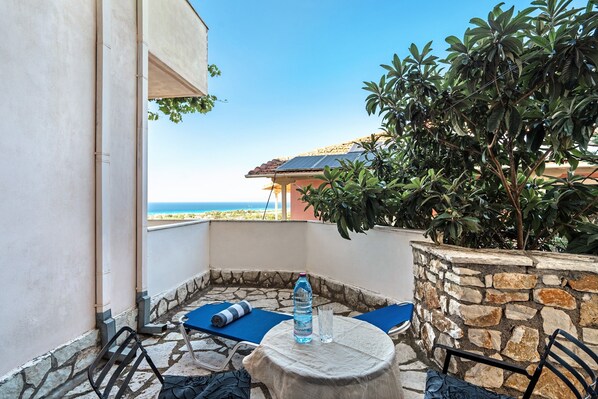 A balcony with a table, chairs, a water bottle, and a view of the sea.