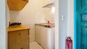 Una cocina compacta con lavavajillas blanco, un armario de madera y una puerta color turquesa.
