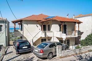 A two-story building with a tiled roof, a balcony, and parked cars.
