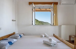 A bedroom with a bed, a window with curtains, a radiator, and a wooden headboard.