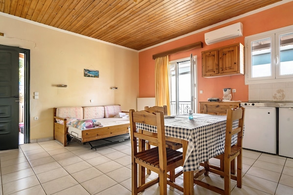 A room with a bed, a dining table with chairs, a kitchen area, and a window with curtains.