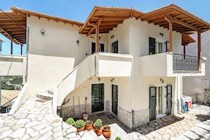 A two-story building with a stone-paved entrance, a wooden balcony, and a door with shutters.