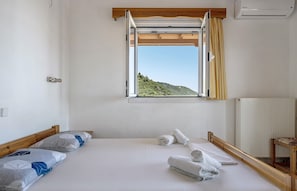 A bedroom with a bed, a window with curtains, a radiator, and a wooden headboard.