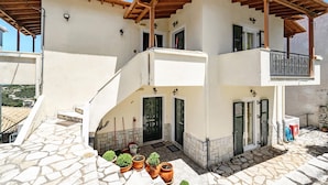 A two-story building with a stone-paved entrance, a wooden balcony, and a door with shutters. - Apartment "Lefkothea 2" with Sea View, Balcony & Wi-Fi (Lefkada)