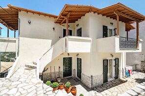 A two-story building with a stone-paved entrance, a wooden balcony, and a door with shutters.
