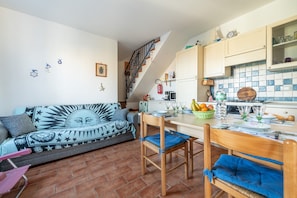 A cozy living room with a sofa, chairs, a dining table, and a kitchen area with cabinets and a tiled backsplash.