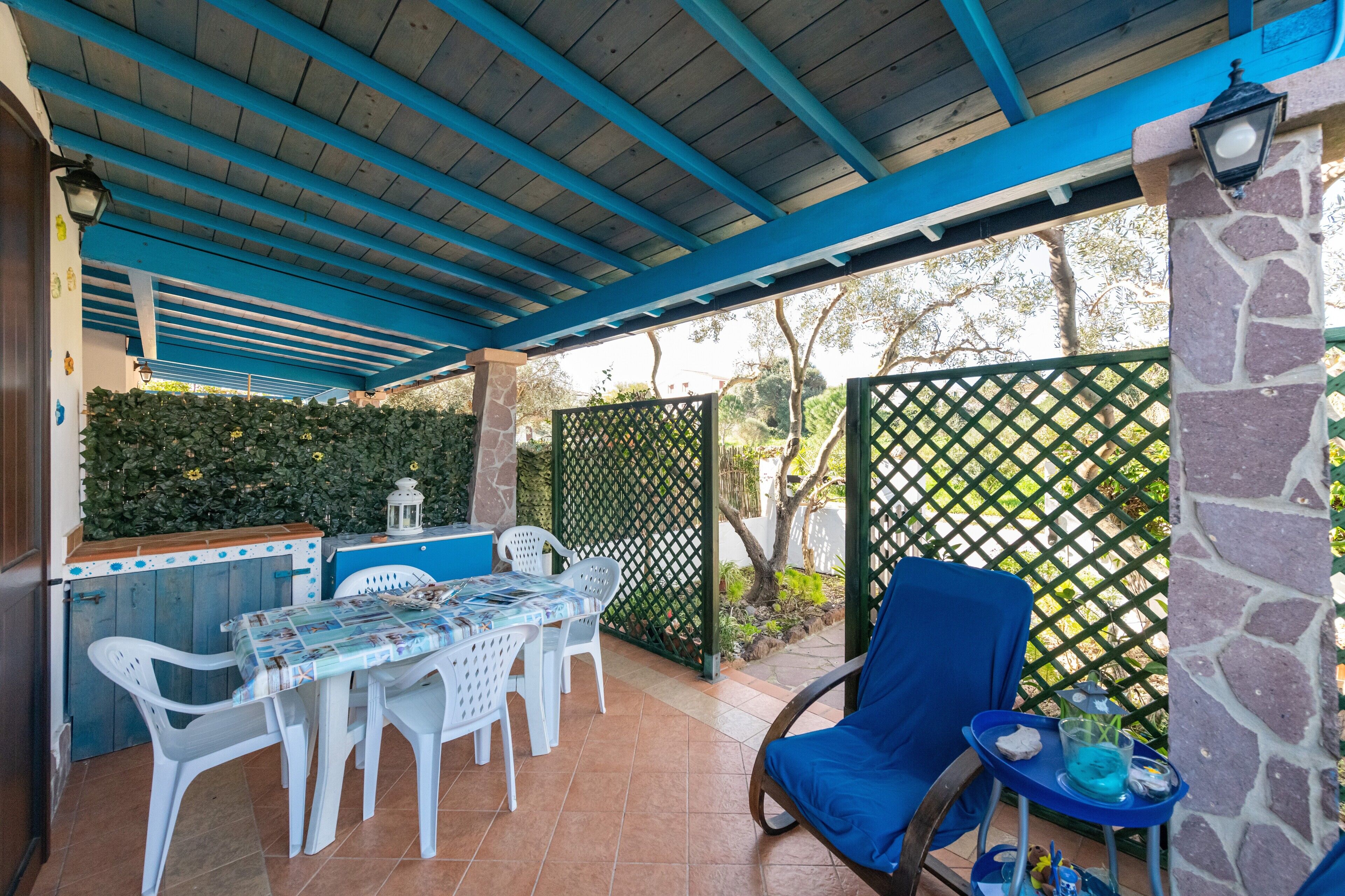 An outdoor patio with a covered area, a table with chairs, a blue chair, and a small table with a drink.