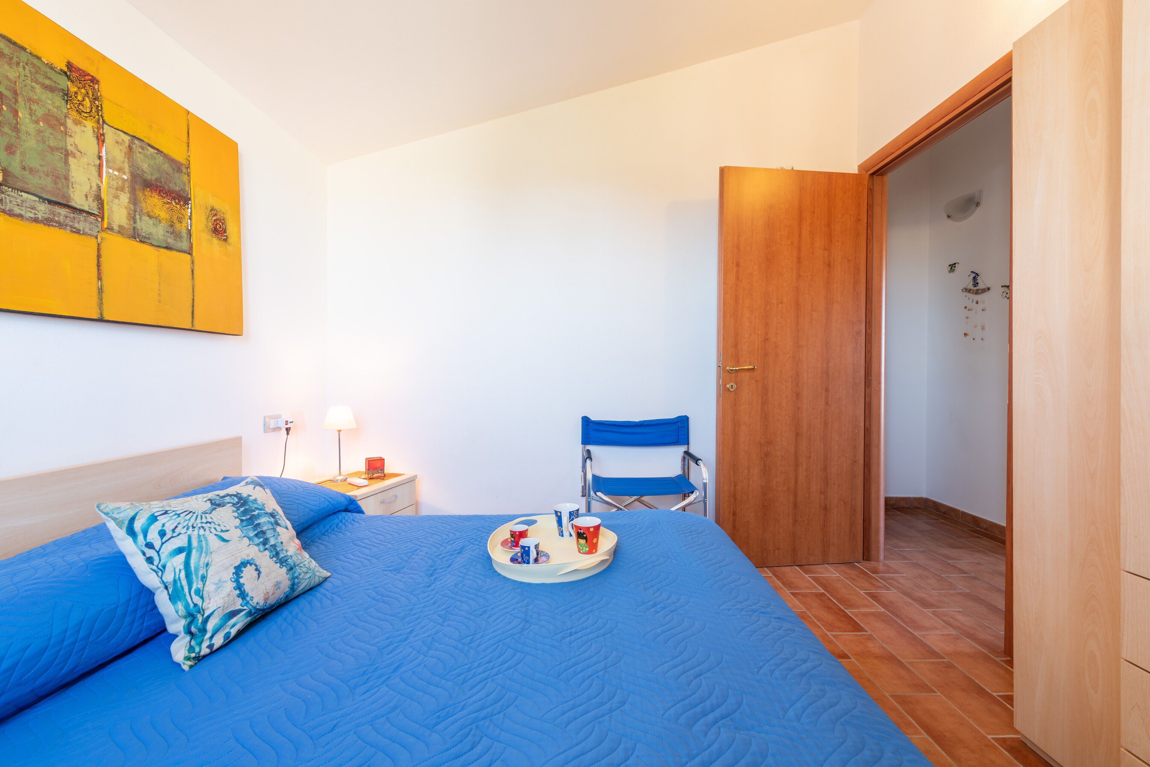 Ein Schlafzimmer mit einem Bett, einem Sessel, einem Tablett mit Gegenständen und einem Bild an der Wand.