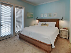 A bedroom with a large bed, two bedside tables, a nightstand, and a window with blinds.
