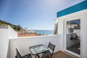 Un balcón con mesa y sillas, un vidrio corredizo y vistas al mar y edificios.