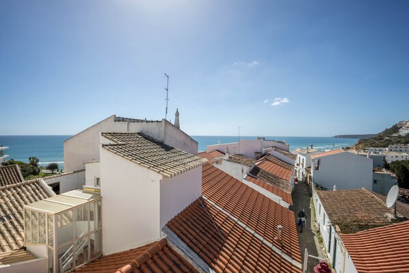 Una zona residencial costera con tejados de tejas de color terracota, cielo despejado y vista al mar.