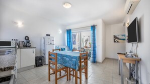 A compact kitchen with a dining area, a TV, and a window with curtains. - Holiday Home "Casa Da Paz" with Sea View, Private Terraces & Wi-Fi (Salema)