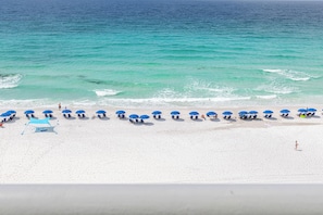 A beach with white sand and turquoise water. There are rows of blue umbrellas and beach chairs.