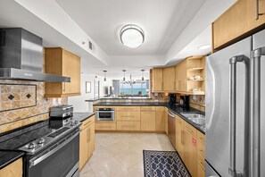 Cozinha moderna com ilha central, eletrodomésticos de aço inoxidável e armários de madeira.