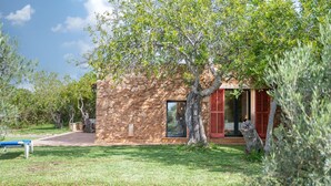 Un edificio de piedra con un árbol en primer plano, un banco y un muro de piedra.
