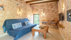 Una habitación con paredes de piedra, un sofá azul, una mesa de centro de madera y sillas de mimbre.