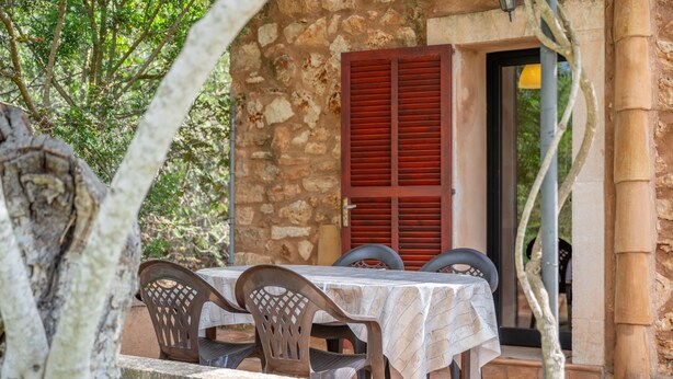 An outdoor dining area with a stone wall, a table with a white tablecloth, and wooden chairs. - Country House 'Andres ' with Mountain View, Wi-Fi and Air Conditioning (Santanyi)