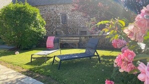 A stone building with a stone roof, two lounge chairs, a red and white striped object, and pink flowers.