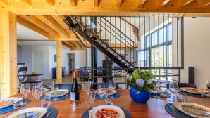 Ein Essbereich mit einem Holztisch, der für eine Mahlzeit gedeckt ist, eine Treppe im Hintergrund und ein großes Fenster, das für natürliches Licht sorgt.