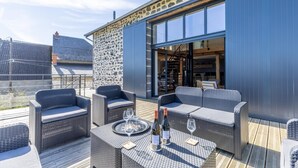 Eine Außenpatio-Terrasse mit Korbmöbeln, einem Esstisch mit Weingläsern und Flaschen sowie einer Steinwand.
