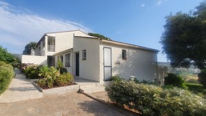 A two-story house with a balcony, a garden with various plants, and a clear sky. - T2 with splendid sea view over the Gulf of Ajaccio and 400m from the beach. (Albitreccia)