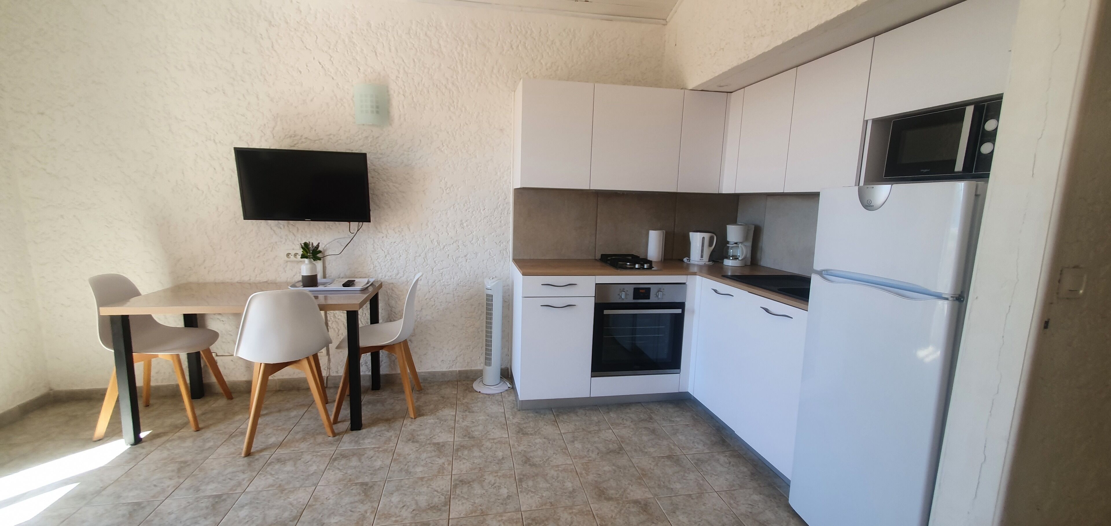 A compact kitchen with white cabinets, a built-in oven, a microwave, and a dining area with a table and chairs.