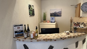 A hotel reception area with a tiled counter, wine bottles, a clock, and framed pictures on the walls.