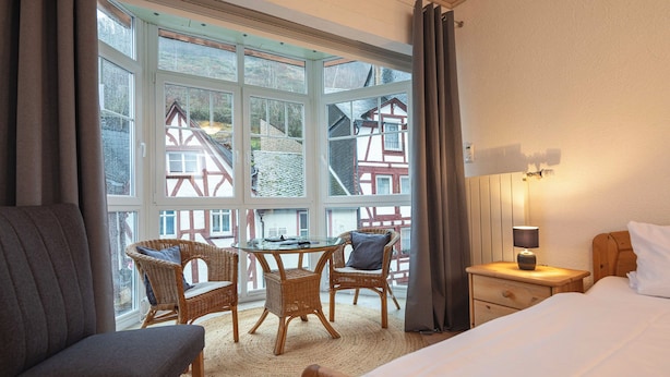 A hotel room with a large window, wicker furniture, a bed, and a nightstand with a lamp.