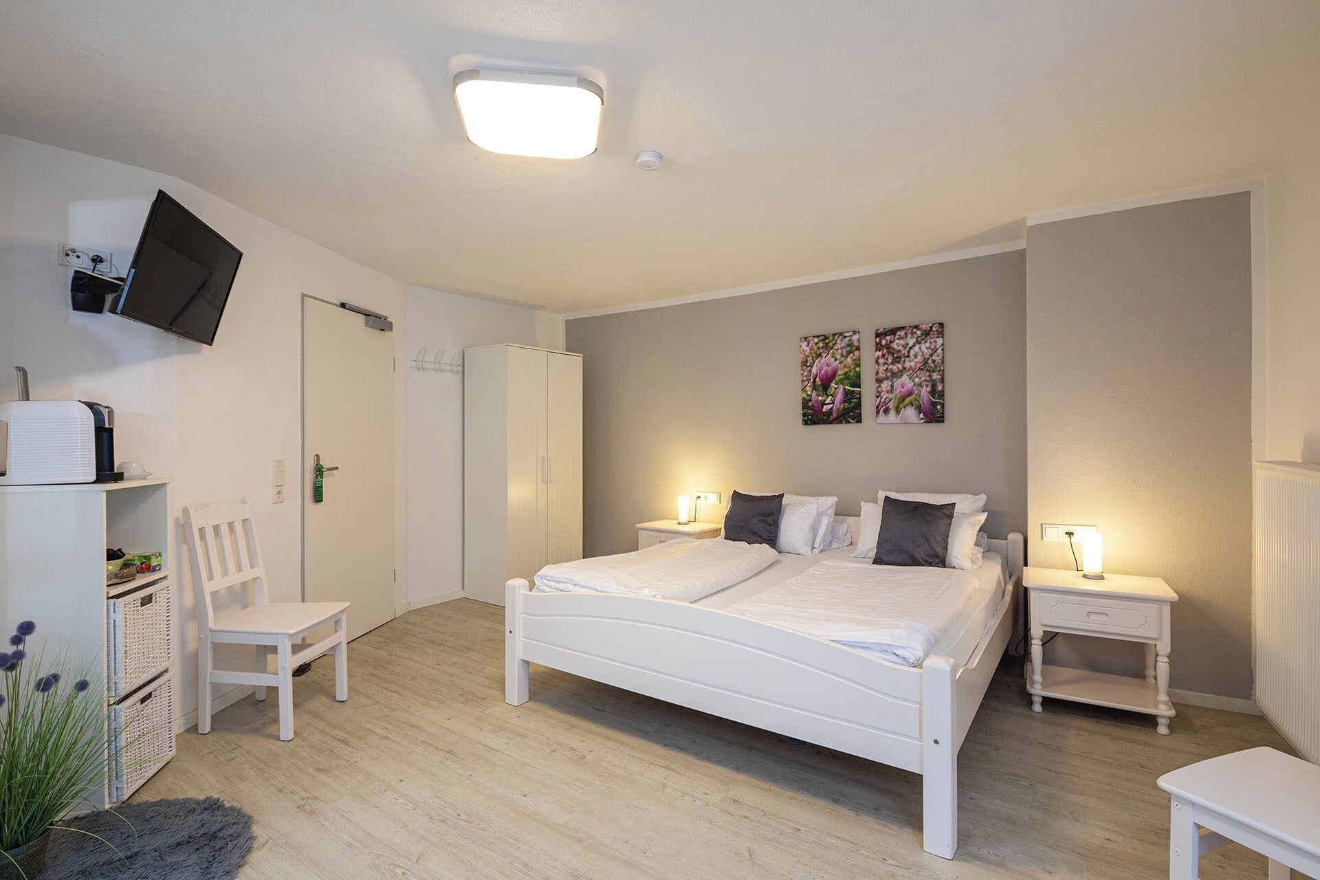 Un dormitorio con cama, mesitas de noche, una silla, armario y televisión de pantalla plana montada en la pared.